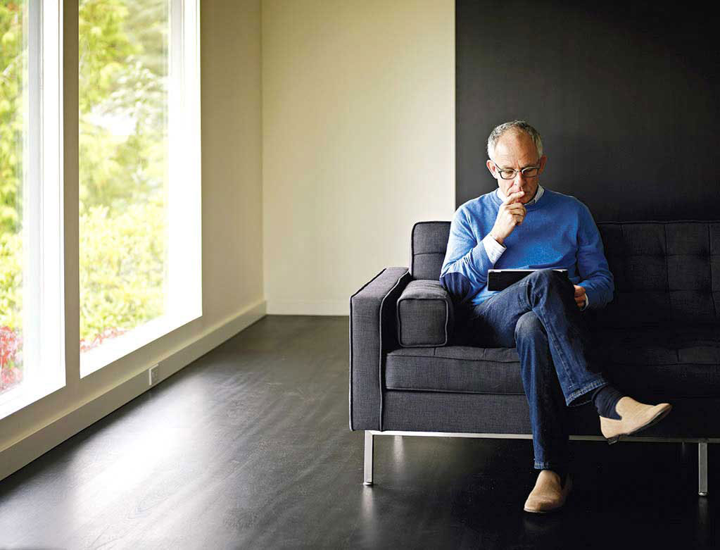 Mature man sitting with legs crossed looking at tablet.