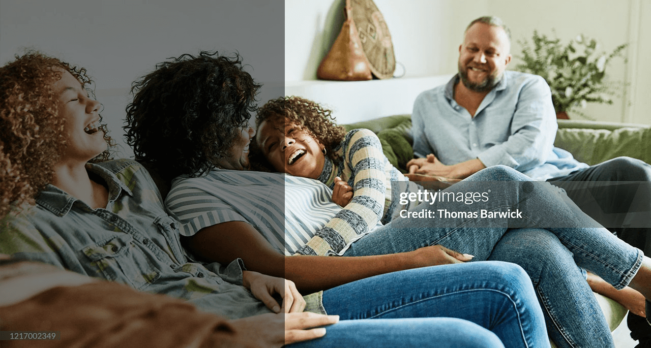 Laughing daughter embracing mother while sitting on couch with family in living room.