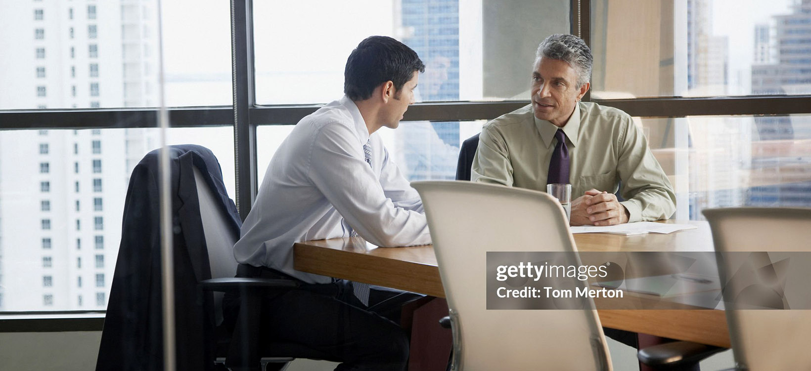 Two businessmen in a boardroom by large windows.