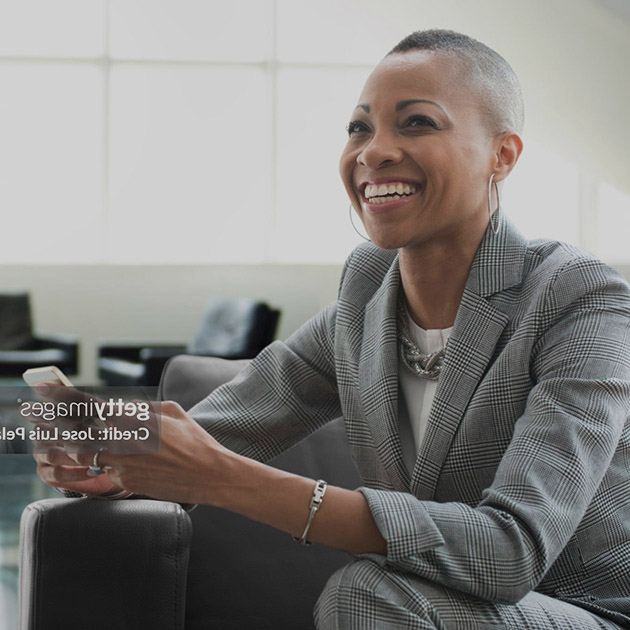 Black businesswoman using cell phone on sofa in office.