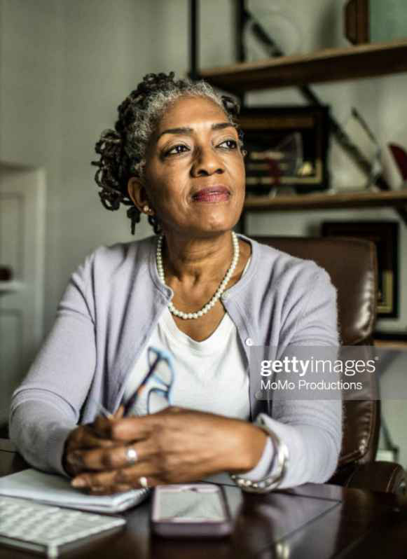 Black businesswoman sitting at desk in home office looking thoughtful.