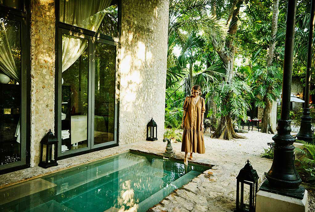 Relaxed woman standing by pool with foot in the water.